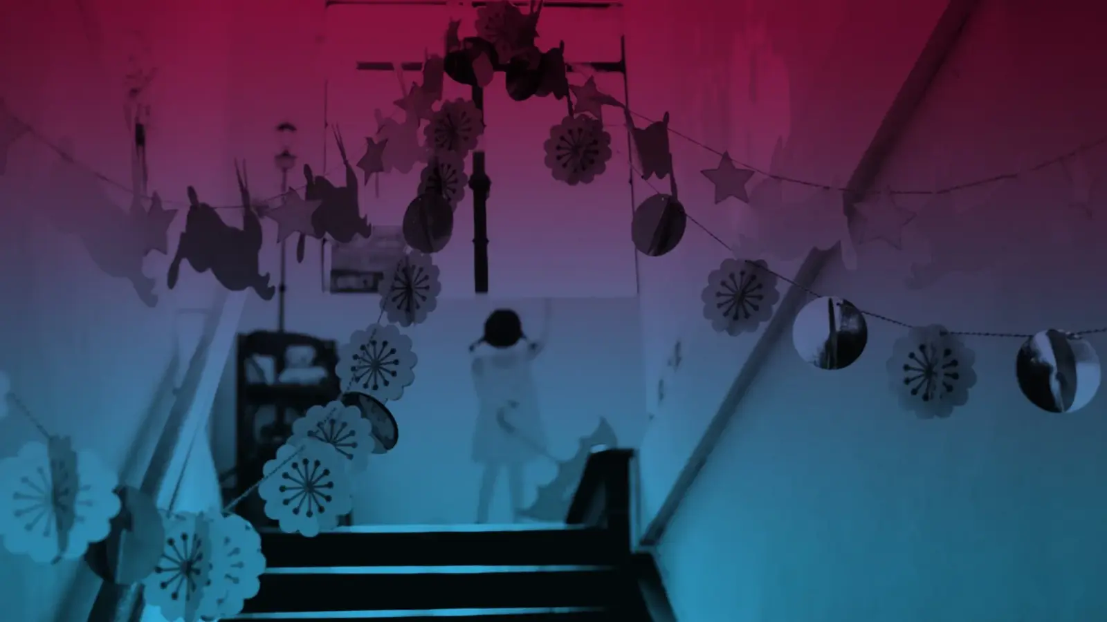 A child standing at the top of a staircase decorated with hanging paper snowflakes and stars, in pink and blue light