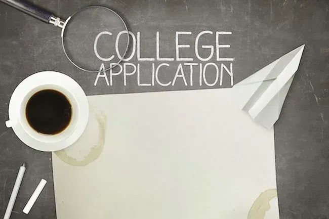 칠판에 분필로 쓴 "COLLEGE APPLICATION" 글씨와 빈 종이, 커피 잔, 돋보기, 종이비행기가 놓인 모습