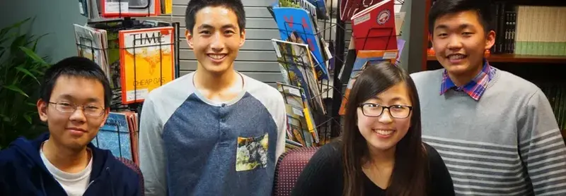 Four smiling students standing together in front of library magazine racks