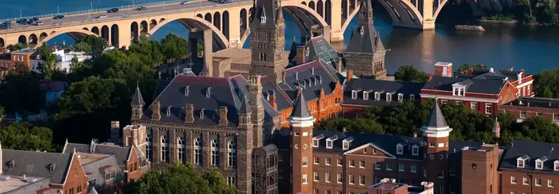 Aerial view of a university campus with stone spires and brick buildings beside a river and arched bridge