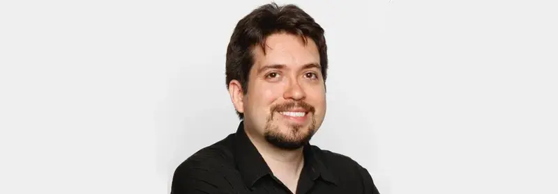 Smiling man with dark hair, goatee and black collared shirt against a plain white background