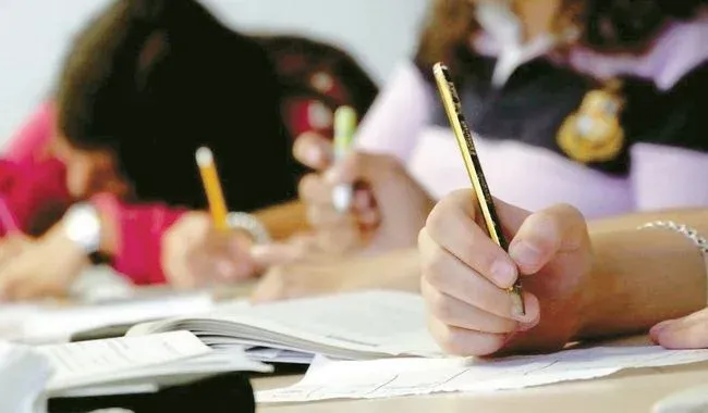 책상에 앉아 연필로 종이와 공책에 글을 쓰고 있는 학생들